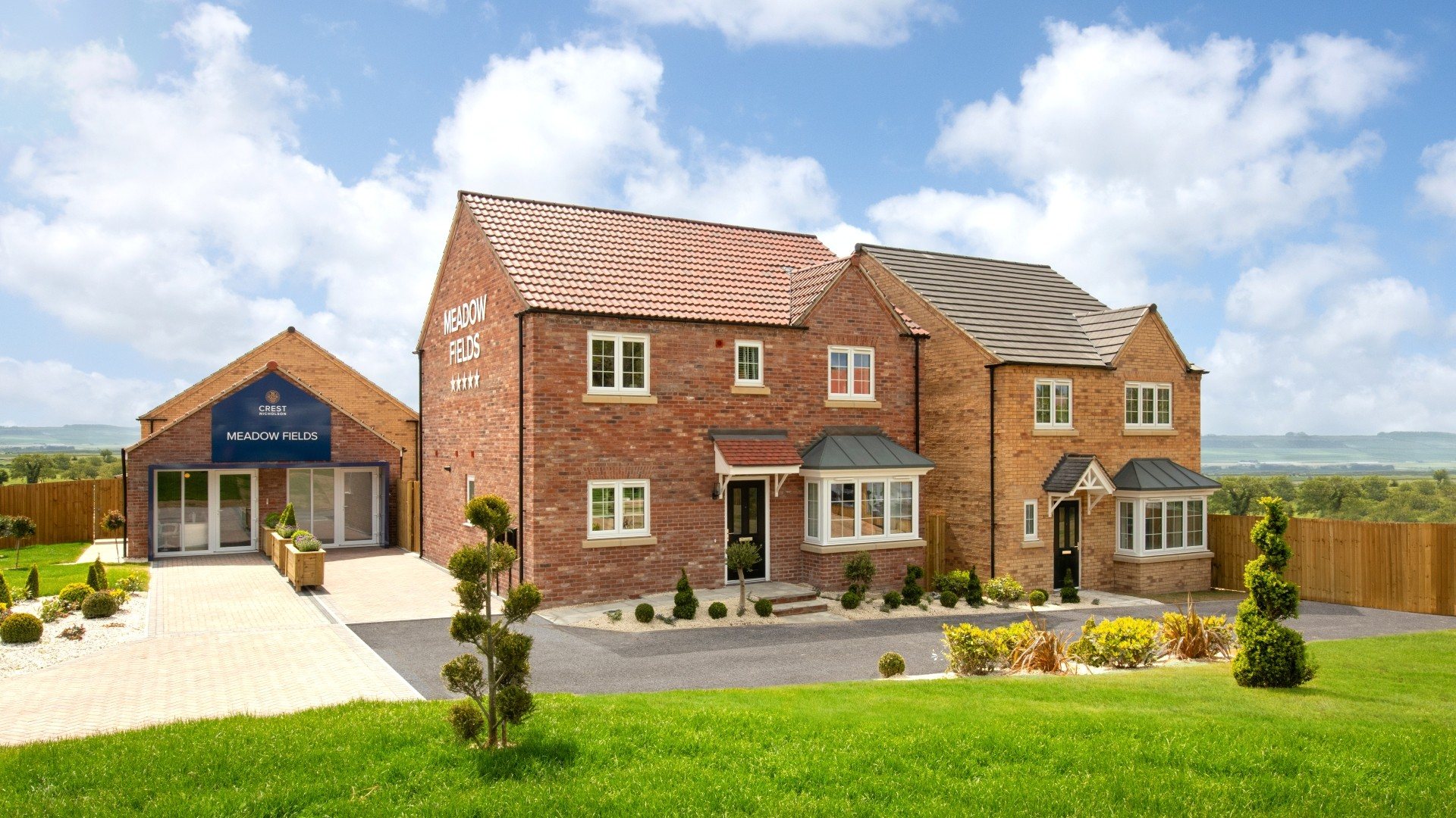 Modern red‑brick detached homes at Meadow Fields in East Ayton, North Yorkshire, overlooking landscaped gardens and open countryside views.