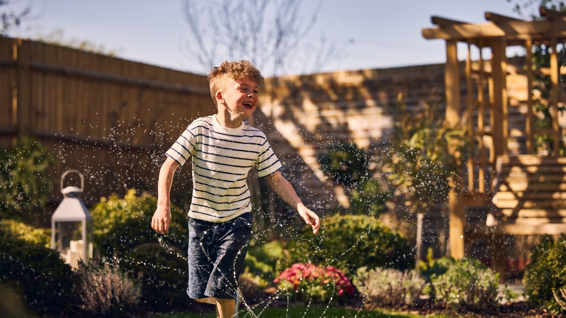Young child playing in the sprinkler in the landscaped garden of a new build Crest Nicholson home